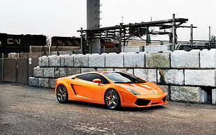 orange Lamborghini sports car parked next to a pile of gray containers HD wallpaper