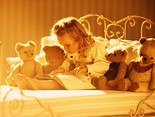 shallow focus photography pf blond haired girl reading book surrounded by brown bear plush toys on bed