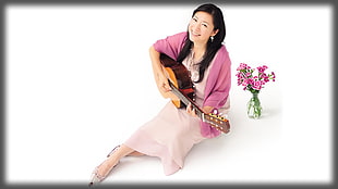 woman wearing pink dress with cardigan playing brown guitar