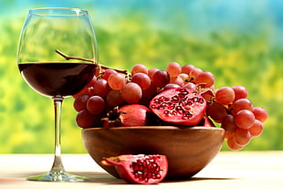 pomegranate and red grapes with wine glass with red liquid on daytime