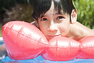 topless boy on pink swimming pool float