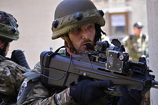 man wearing green, white, and black military suit holding assault rifle during daytime