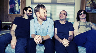 photo of four men sitting on blue sofa