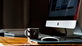 coffee cup near silver iMac on wooden desk