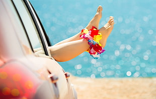 person with multicolored petaled flower anklet lying inside vehicle near sea