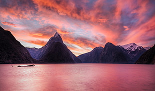 photo of boat on body of water near mountains during dawn time