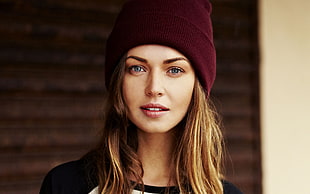 woman wears maroon knit cap and crew-neck shirt near brown wall