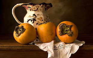 several Persimmon fruits near white and multicolored flower painted ceramic pitcher