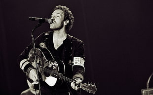 photo of man playing acoustic guitar in front of mic