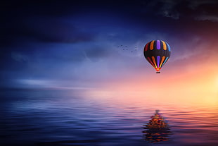 multi color hot air balloon above body of water during sunset