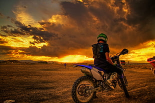 photo of man riding motocross dirt bike under nimbus clouds