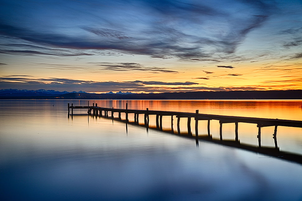 silhouette of sea dock on calm sea under golden sky HD wallpaper