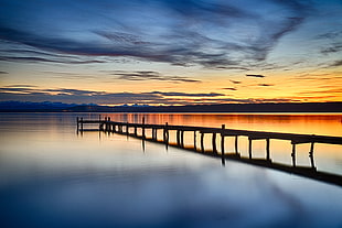 silhouette of sea dock on calm sea under golden sky HD wallpaper