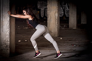 woman in black sleeveless top and gray leggings doing exercises inside gray establishment