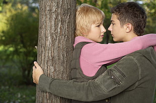 blonde girl and black haired boy hugging near tree