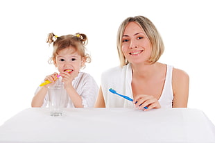 woman holding a blue toothbrush sitting next to a girl