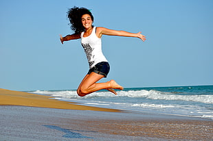woman jumping on white sand beach HD wallpaper