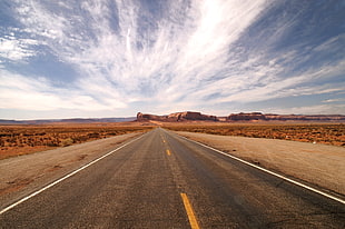 asphalt road in the middle of the desert under white clouds and blue sky during daytime HD wallpaper