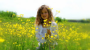 girl standing holding yellow petaled flowers wearing white jacket and tank top