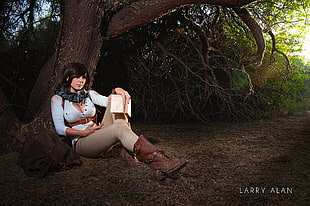 woman wearing white button-up shirt and brown boots lying near tree