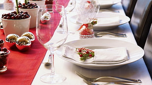 closeup photography of plate, spoon, fork and clear wine glass on table with white and red table clothes