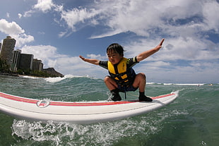 boy wearing black and brown vest while standing on white and red surfboard