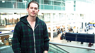 man wearing black and green plaid zip-up hoodie standing next-to concrete building during daytime