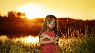 girl in red dress surrounded by green grass during yellow sunset