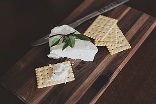 four rectangular soda crackers and white cheese on brown wooden board