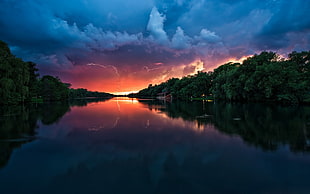 body of water between green trees under cloudy blue sky