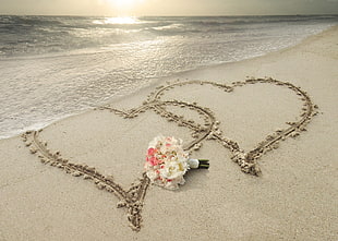 white and pink chrysanthemums bouquet on white sand with two hearts on seashore at daytime