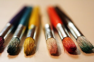 depth of field photography of six assorted painting brushes on top of beige surface