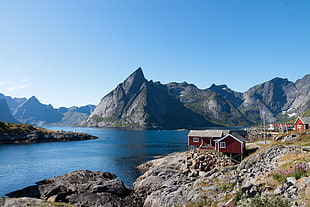 red wooden house near body of water surrounded with mountains
