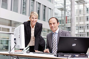 man in black blazer standing beside man in gray suit with laptop and computer monitor