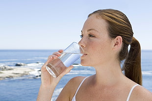 woman drinking fresh water on glass cup during day time on the beach HD wallpaper