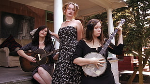 woman standing between two women holding string music instruments