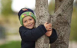boy holding on gray tree branch while smiling