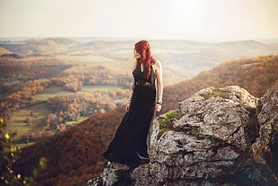 red haired woman wearing black dress standing on rock