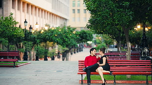 man and woman sitting on red bench talking to each other