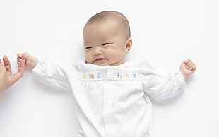 baby in white long-sleeved shirt holding person's index finger