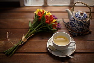 photography of white ceramic teacup set; blue and white ceramic teapot; and red and yellow petaled flowers, tea, flowers