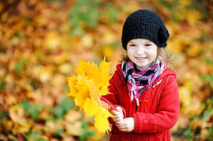 girl wearing red jacket and black beanie holding brown maple leaf