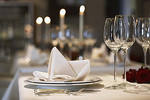selective focus photography of white table napkin on white ceramic plate near wine glasses