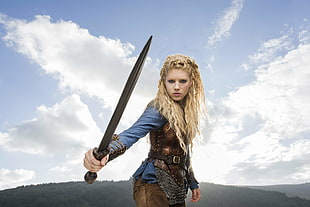 female wearing blue long-sleeved shirt and brown armor holding sword movie character