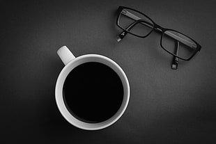 white ceramic mug filled with coffee near black frame eyeglasses