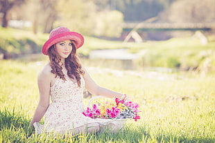 woman in yellow floral dress sitting on green grass holding basket with flowers