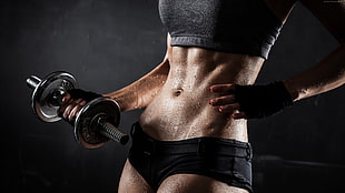 woman wearing black sports brassiere and under while holding dumbbells