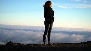 black haired woman in black jacket standing on brown mountain during daytime HD wallpaper