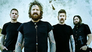 four men wearing black shirts standing near on concrete wall
