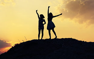 silhouette of two girls with hands up during yellow sunset HD wallpaper